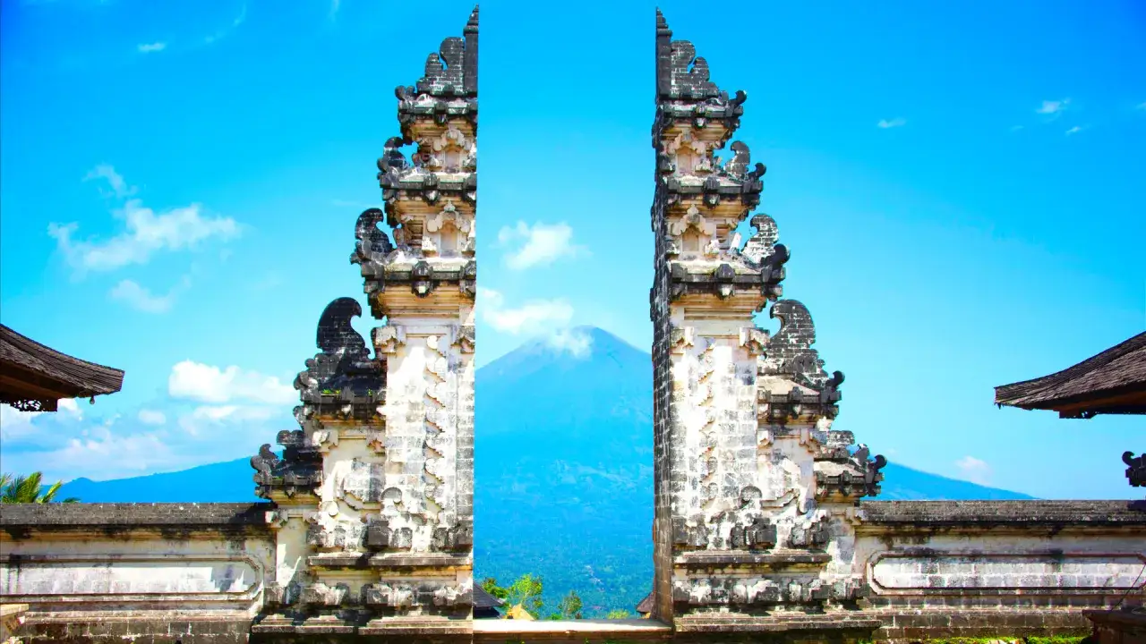 Porte d'un temple balinais avec un volcan en arrière-plan sous un ciel bleu éclatant.