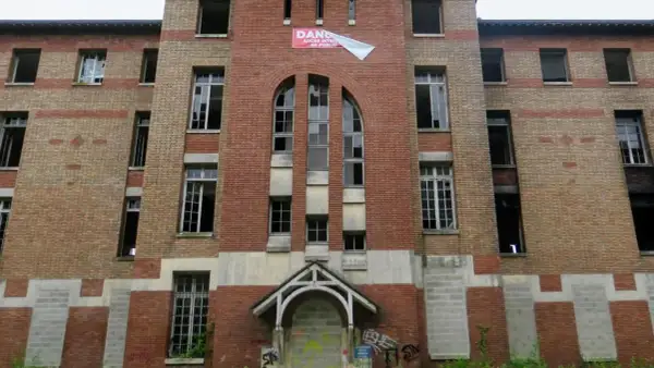 Façade imposante de l'hôpital abandonné d'Angicourt, avec ses fenêtres brisées et un panneau "DANGER ACCÈS INTERDIT AU PUBLIC".